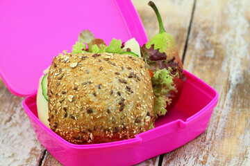 Lunchbox containing whole grain roll with Swiss cheese, lettuce and cucumber and pear
