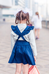 Obraz premium A girl in a school uniform with a backpack on her back stands with her back to the camera