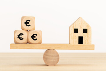 Home purchase concept. Wooden toy house and wooden dice with euro symbol text on seesaw