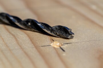 A closeup portrait of a wooden plank with a hole drilled into it on the intersection of a pencil marking with the wood drilling bit lying next to it. The marking is a cross drown in pencil.