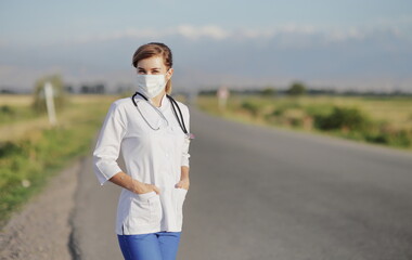 Female doctor or nurse wearing a protective face mask next to a rural road.