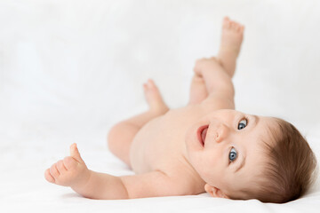 Cute smiling baby lying on white bed looking back at camera