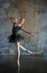 young ballerina in a black suit and black pointe shoes, dancing against the background of a textured wall, froze in a graceful pose