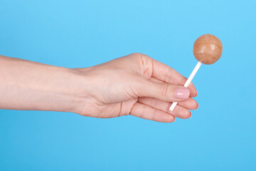 Hand with sweet caramel lollipop. Isolated on blue background.