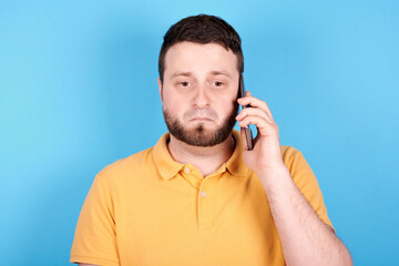 Brunette man using mobile phone and scared. Isolated on blue background.
