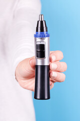 Hand with nose trimmer, hair electric cutter. Isolated on blue background.