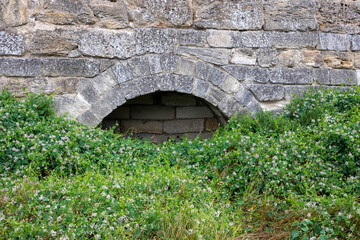 A small arch overgrown with grass in the fortress wall.Old ruins