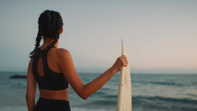 Surfer girl standing with board and looking on the Pacific ocean, mind setting before surfing training