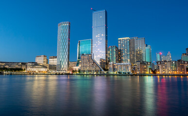 Financial district of London city Canary Wharf reflected on the Thames river at blue hour in England
