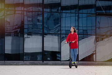 Cute teenager girl riding electric kick scooter in a cityscape         