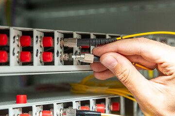 A man inserts a yellow fiber optic cable into a switch. Hands close up. Horizontal orientation. 