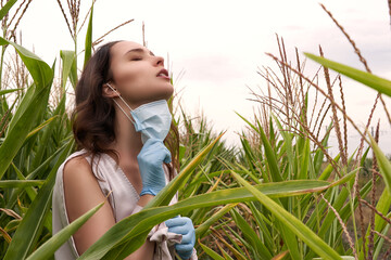 Beautiful girl with protective mask on face and medical gloves in cornfield. Coronavirus epidemic, COVID-19 quarantine concept