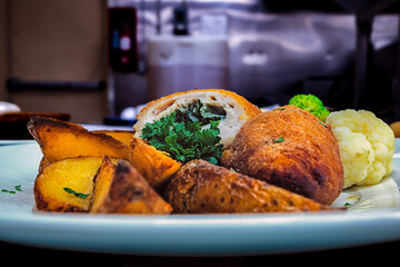 Close up of a serving of Chicken Kiev with vegetables and potato wedges.
