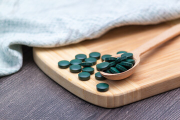Green tablets - spirulina or chlorella in a wooden spoon. Healthy living concept.