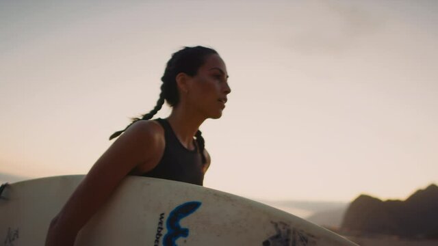Close up of surfer woman walking out of Pacific ocean with board, training in evening, tired but pleased