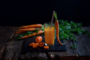 Carrot juice in a glass glass with lots of carrots on the table. Vitamin A in vegetables. Rustic style