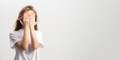Beautiful young woman covers face with hands, isolated on a gray background