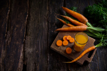 Carrots and carrot juice on a dark wooden table with a place for text in a rustic style. Vegetables from the garden