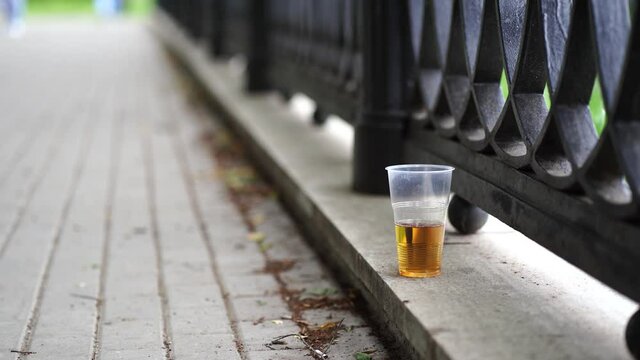 Close up of disposable cup with beer stands on concrete on waterfront. Alcoholic beverage forsaken in public park.
