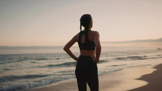 Sportswoman walking away by the beach, mind setting for a training, sunset over Pacific ocean