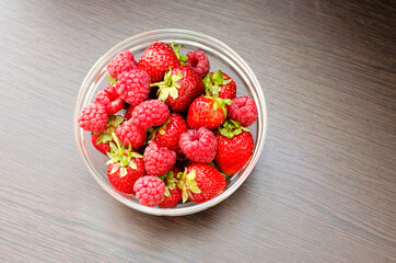 Transparent bowl with strawberries and raspberries close-up top view