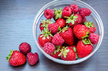 Transparent bowl with strawberries and raspberries close-up top view.