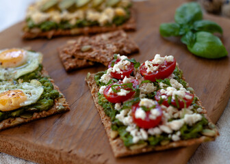 Avocado Toast with cherry tomatoes greek cheese and a basil twig. Colorful avocado toast over a wooden cutting table. Rustic mood.