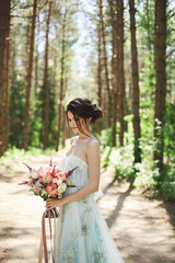 Side view of an adorable young lady in a long summer dress with a big bouquet of flowers in her...