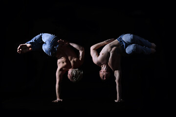 two twin brothers in blue jeans with a naked torso perform acrobatic elements, black background