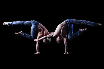 two twin brothers in blue jeans with a naked torso perform acrobatic elements, black background