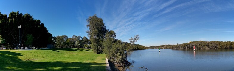 Fototapeta na wymiar Beautiful panoramic view of a river with reflections of blue sky, light clouds and trees on water, Parramatta river, Rydalmere, New South Wales, Australia