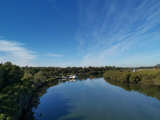 Fototapeta na wymiar Beautiful view of a river and a wharf with reflections of blue sky, light clouds and trees on water, Parramatta river, Rydalmere, New South Wales, Australia