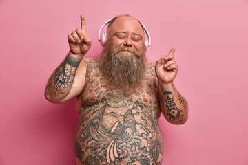 Handsome relaxed obese overweight man dances to music in headphones, enjoys every bit of song,...