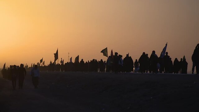 KARBALA, IRAQ - NOV 2017: Silhouette of crowd of pilgrims walking in Arbaeen pilgrimage at sunrise. Every year, millions of Shiite muslims come from all over the world to Karbala to walk Arbaeen