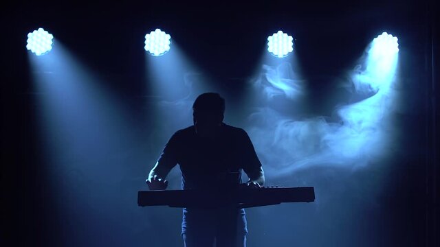 Musician silhouette playing on synthesizer piano keyboard in dark studio with neon lighting. Neon lighting effects. Performance vocal and musical band.