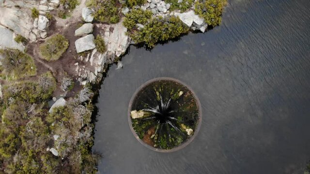 Aerial drone rotating over big sinkhole constructed as a water spillway at Covao dos Conchos dam lake in Serra da Estrela