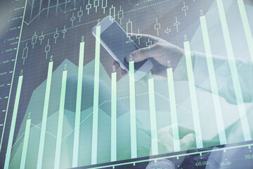 Double exposure of man's hands holding and using a digital device and forex graph drawing. Financial market concept.