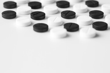 Close up of black and white pills lie exactly in a row on a white table with copy space for text. Isolated pharmaceutical drug minimalistic background