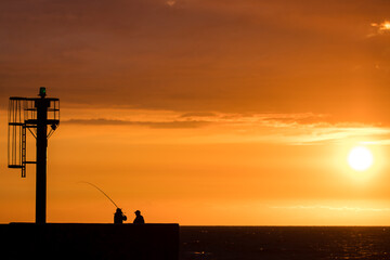 Silhouettes of anglers casting a fishing rod against the backdrop of the sunset over the Baltic Sea in Ustka.