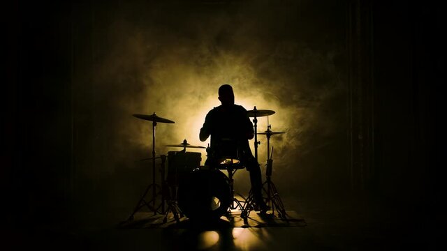 Silhouette drummer playing on drum kit on stage in a dark studio with smoke and neon lighting. Performance vocal and musical band. Slow motion.