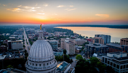 Wide aerial shot of a dramatic, fiery sunrise over the Wisconsin State Capitol. Statue atop the dome appears to hold the rising sun. - obrazy, fototapety, plakaty