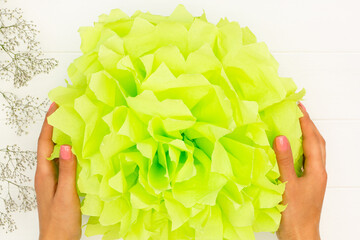 Step by step tutorial. Green fluffy pom-pom from tissue paper on a white wooden table background....