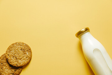 Two cookies and a bottle of milk over a yellow wallpaper