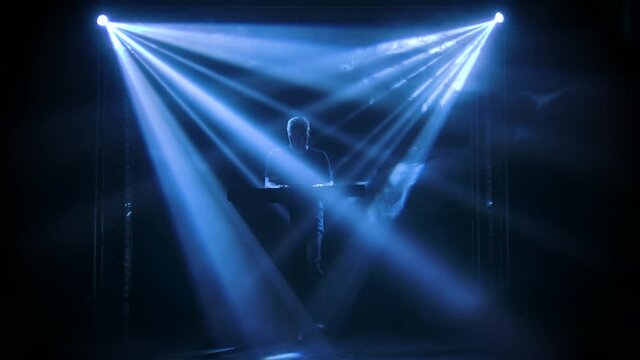 Musician silhouette playing on synthesizer piano keyboard on stage in a dark studio with smoke and neon lighting. Dynamic neon lighting effects. Slow motion.