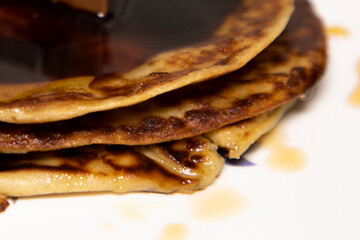 Banana Pan Cake garnished with Chocolate Syrup and Choclate Cube at the top served on white ceramic plate
