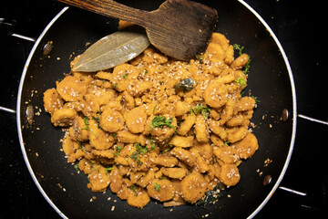 Gattey ki sabji Indian Delicious Cuisine of Rajasthan made with Roasted Boiled Gram Flour mixed with Seasame Seeds and Cumin Seeds in Glass bowl and Frying Pan decorated with Leaf Spatula
