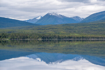 Wilderness woods, forest with lake reflection & snow capped mountains in the summertime. Taken in northern Canada. 