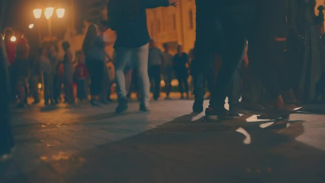 Street salsa dance in the night, many defocused young couples dance social latino dances in slow motion, ground level view with copyspace on foreground