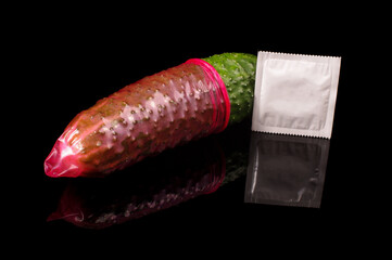 Pink condom pulled on cucumber isolated on the black