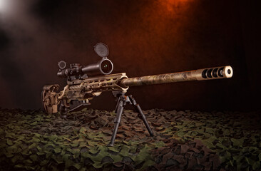 Dark, smokey background in a studio of a sniper rifle on a camouflage net.